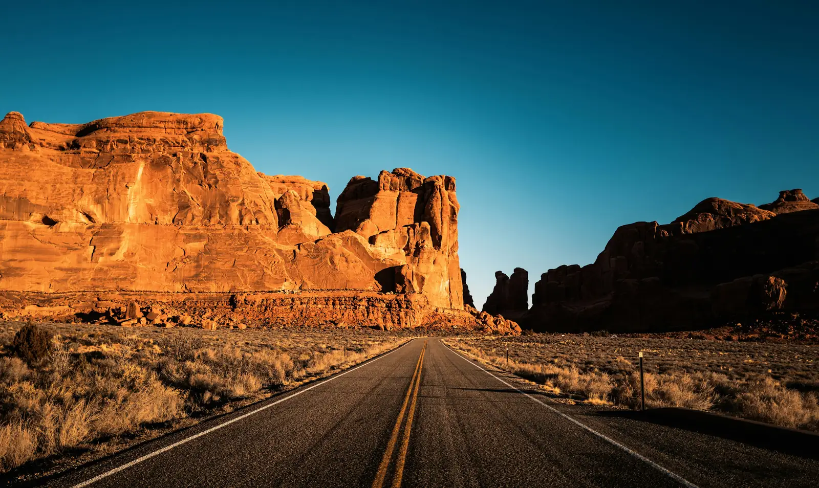 Empty desert highway running between golden sandstone buttes in Arches National Park